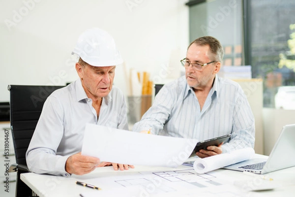 Fototapeta Engineers planning a construction project with blueprints, tablets, and hardhats. Concept of teamwork, architecture
