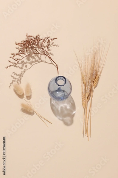 Fototapeta Glass vase with dried flowers on beige background with shadow from sunlight. Minimalistic aesthetic still life. Top view