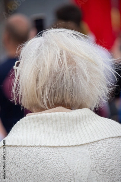 Fototapeta A woman with a white sweater and glasses is sitting in a crowd
