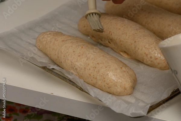 Obraz A woman gently brushes homemade Graham loaves with egg wash before placing them in the oven.