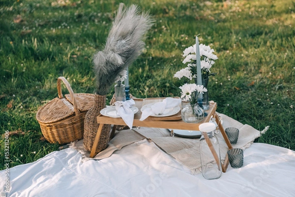 Fototapeta Elegant picnic setup on lush green grass with decorative flowers and unique tableware