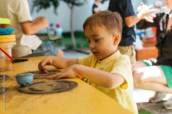 Obraz Boy playing with sand and pretend outdoor kitchen during summer daycare playtime. Imaginative and sensory activity for toddlers