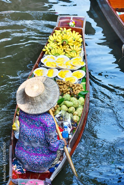 Fototapeta A vendor is rowing a boat to sell fruit in a canal at Damnoen Saduak Floating Market, the most famous floating market in Thailand.