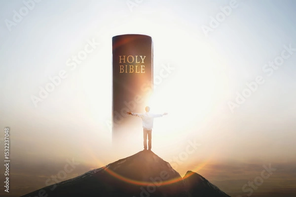 Obraz Christian standing with arms raised on top of a high mountain, praising and praying, looking at the holy bible and the cross of Jesus Christ with love in the background
