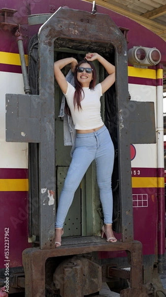 Obraz Stunning Asian woman in denim and heels, rocking a fierce pose in a passanger train wagon’s frame