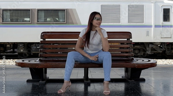 Obraz Striking a stylish pose, fit Asian woman in jeans, heels and a white top sits on a bench at the train station