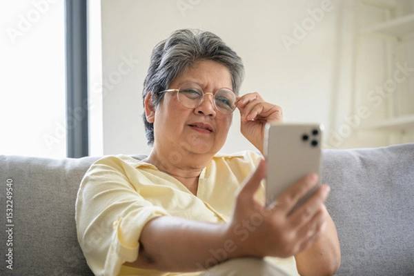 Fototapeta Senior people lifestyle health problem concept : Portrait photo of senior Asian woman has an eye long sighted problem trying to read message from smartphone monitor.
