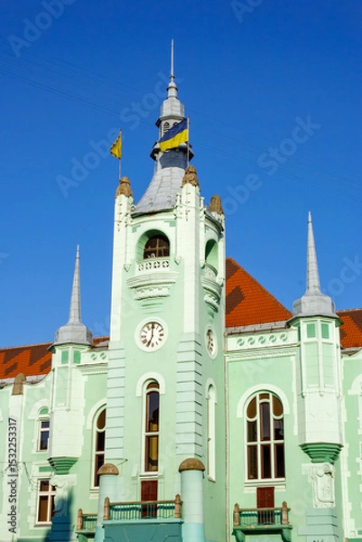 Fototapeta mukachevo, ukraine - jun 16 2012: city council of the old town in morning light. green building with clock tower. popular travel attraction in the city center. empty street in summer. blue sky