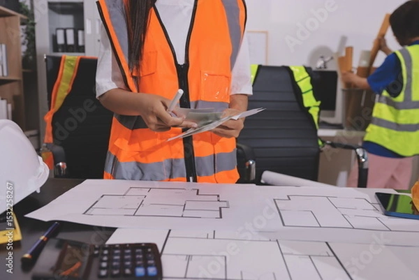 Fototapeta Closeup of team of industrial engineers meeting analyze machinery blueprints consult project on table in manufacturing factory. Working in manufacturing plant or production plant.