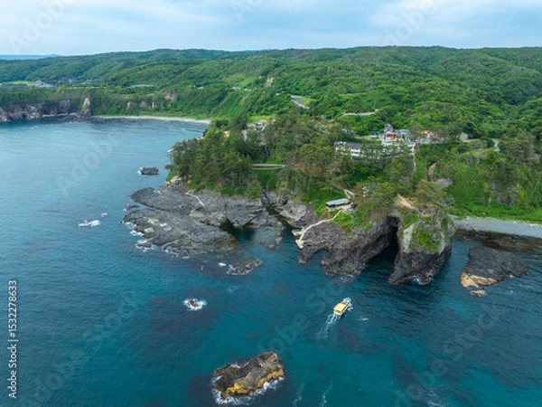 Obraz 石川県能登半島の名所・巌門にある自然の海蝕洞に、遊覧船が進入する様子をドローンで撮影。断崖と日本海の荒波が生んだ壮大な地形を捉えた空撮写真。