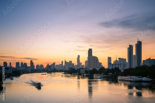 Fototapeta Sunrise view of the Chao Phraya River with skyline silhouettes modern high-rises, as a boat moves through golden reflections.