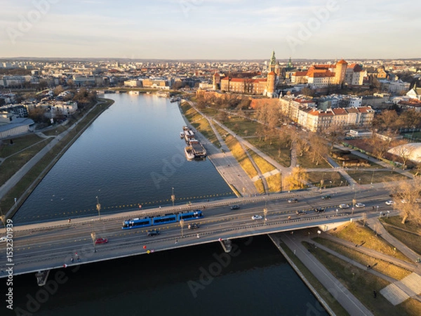 Fototapeta Krakow, Poland: Aerial view  of a tramway driving on a bridge over the Vistula river with the famous Wawel Royal Castle in the background on a sunny winter day in Poland.