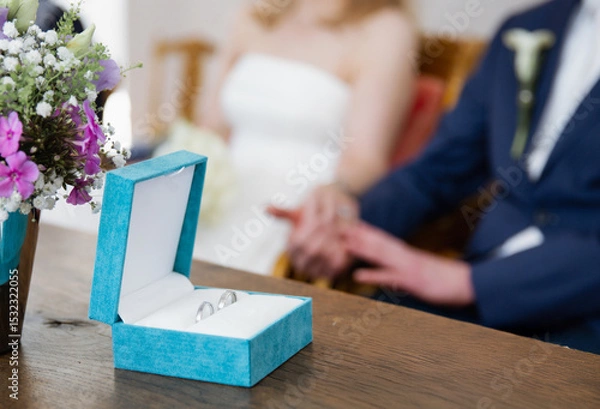 Obraz Close up of a blue box with two silver wedding rings on a wooden table, blurred background 