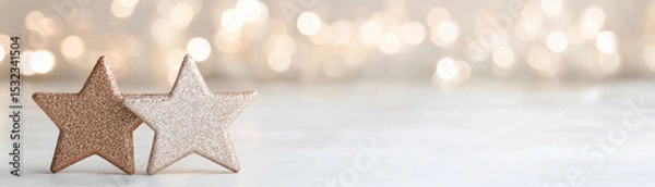 Fototapeta Two glittery star shaped ornaments in warm golden tones with soft bokeh lights creating festive and cozy atmosphere