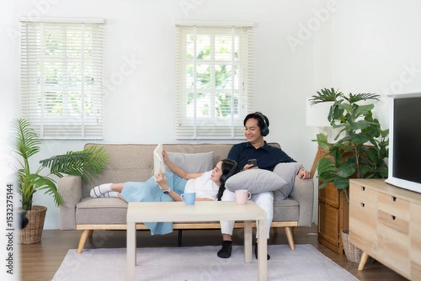 Fototapeta Couple enjoying cozy time at home, relaxing on sofa with technology