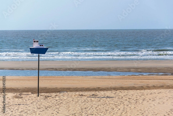 Obraz Wooden model of a blue and white boat on pole on a sandy beach, coastal village De Haan, West Flanders, Belgium