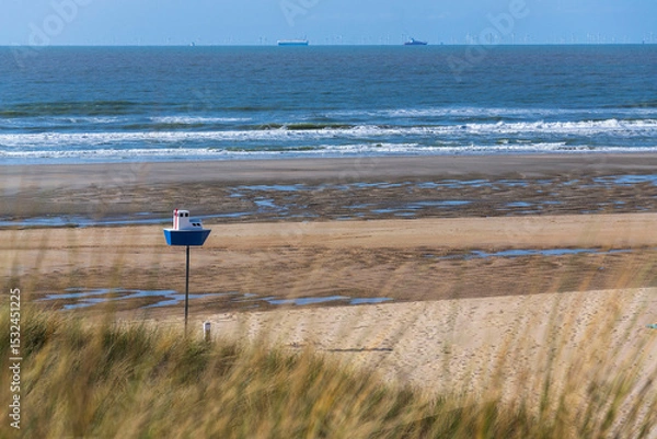 Obraz Wooden model of a blue and white boat on pole on a sandy beach, coastal village De Haan, West Flanders, Belgium