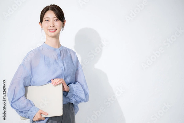 Fototapeta 白背景でパソコンを持つ水色のシアーシャツの女性のカメラ目線　転職や人事などのリクルートのイメージ