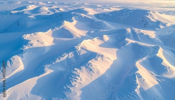Fototapeta Aerial view of snow-covered mountain range in Antarctica illuminated by the soft glow of sunrise, creating a serene and majestic polar landscape.