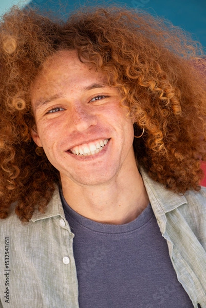 Fototapeta Vertical close-up portrait of smiling young man with curly hair and freckles against colorful wall. Youthful student, personal branding, modern lifestyle and fashion concept.