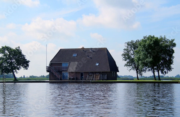 Fototapeta House and trees at a lake against blue sky with white clouds (Giethoorn, Netherlands)