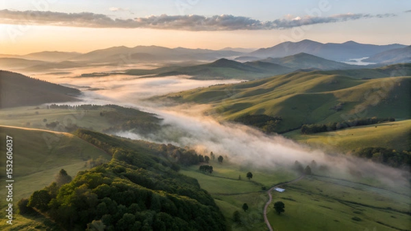 Obraz Aerial view of forested mountain peaks emerging from a thick sea of clouds at sunrise. The soft mist flows between the hills, creating a surreal, dreamlike atmosphere with warm light on the horizon. P