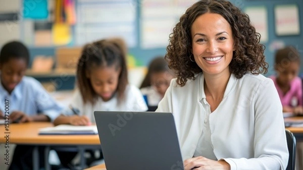 Fototapeta A cheerful woman smiles at the camera while working on her laptop, surrounded by engaged children in a vibrant classroom setting, promoting a positive learning environment.