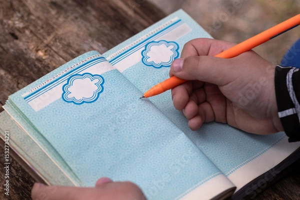 Fototapeta A child writes in a vintage diary with blue pages using an orange pen