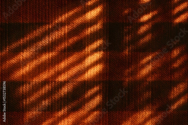 Fototapeta Diagonal shadows from window blinds falling across a red plaid wool textile, creating a warm textured pattern..