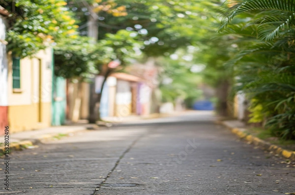 Fototapeta Defocused image of a quiet Urban Street Lined with Trees and Colorful Houses, Suggesting Peace, Simplicity, and Everyday Life in a Sunny Neighborhood. To be used as background