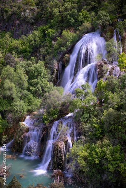 Fototapeta cascade falling through the lush vegetation, Campillo waterfall, in the natural park of the Alto Tajo in Guadalajara, vertical