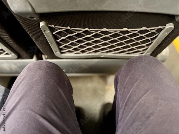 Obraz Two passengers are sitting in an armchair with a narrow footway in the economy class cabin of the bus. View of the legs from above. People in transport, close-up
