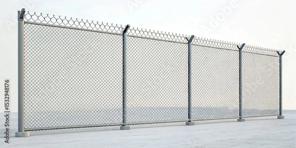 Fototapeta A chain link fence with barbed wire on top, supported by metal posts on a concrete surface. The background features a pale, overcast sky.