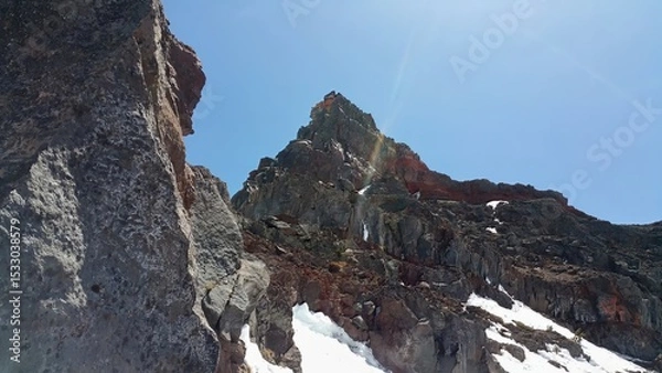 Obraz Low angle view of a rocky mountain peak with patches of snow under a clear blue sky on a sunny day