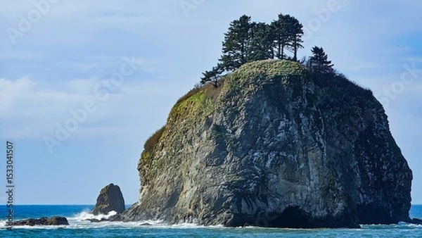 Obraz A large rock formation with trees on top surrounded by ocean water under a bright blue sky day light
