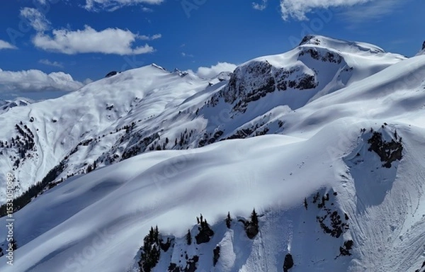 Obraz Snowy mountain range under a bright blue sky with scattered clouds on a clear sunny winter day