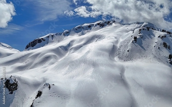 Obraz An aerial view of a snow covered mountain range under a blue sky with scattered white clouds above it