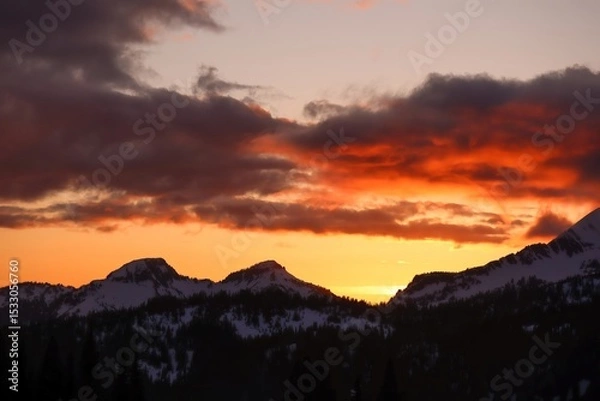 Obraz Sunset over snowy mountain peaks with orange and gray clouds filling the sky at dusk in a scenic view