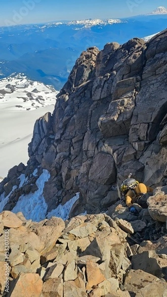 Obraz A climber ascending a rocky mountain ridge with snow patches and distant mountain range under a blue sky