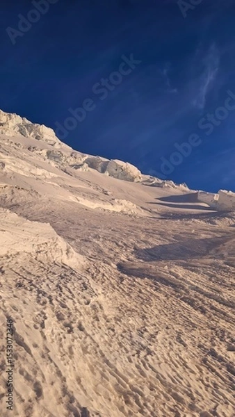 Obraz A snowy mountain slope under a clear blue sky showcasing textures and patterns of snow and ice formations