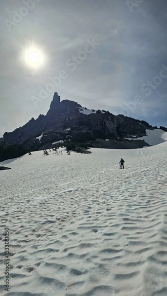 Obraz Person hiking on a snow covered field towards a rocky mountain under a bright sunny sky outdoor view