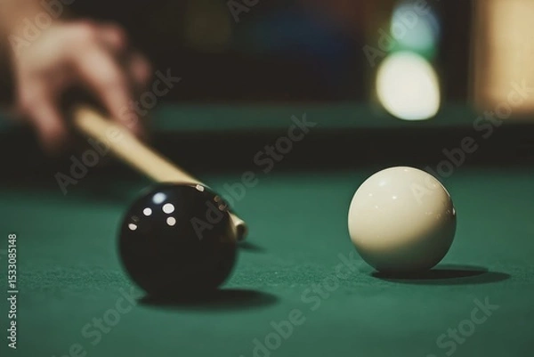 Fototapeta A person is playing pool, holding the white ball in one hand and rolling it towards another black sphere placed in front of them on a green felt cloth Generative AI