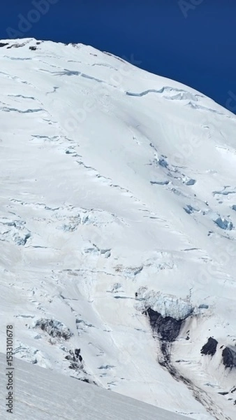 Obraz A view of a snow covered mountain under a clear blue sky with visible crevasses and rock formations