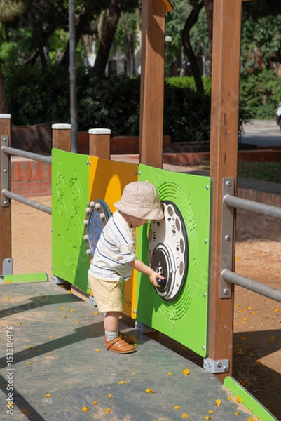 Obraz Baby playing outdoors on little kids playground. The child using both hands to explore the panel witch features musical symbols and a circular, interactive component resembling a control dial. 