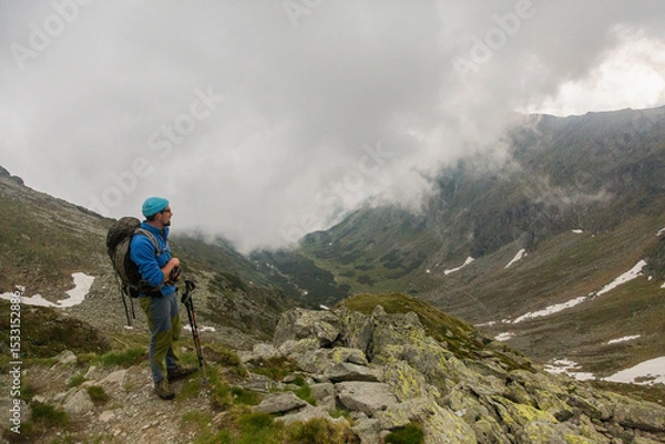 Fototapeta Adventure enthusiast hiking through dramatic rocky wilderness, using poles for stability while crossing steep terrain dotted with massive stones
