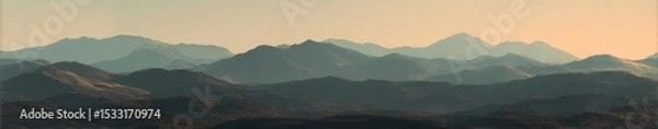 Fototapeta Soft-focus panorama of a hazy mountain range at dawn or dusk, showing layers of muted blues and browns