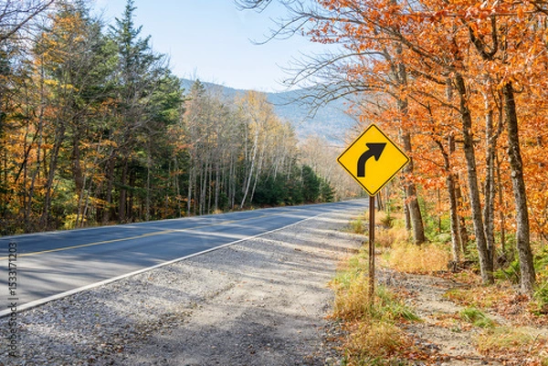 Fototapeta Yellow traffic sign warning drivers agaisnt a dangerous curve along a mountain road on a sunny autumn day