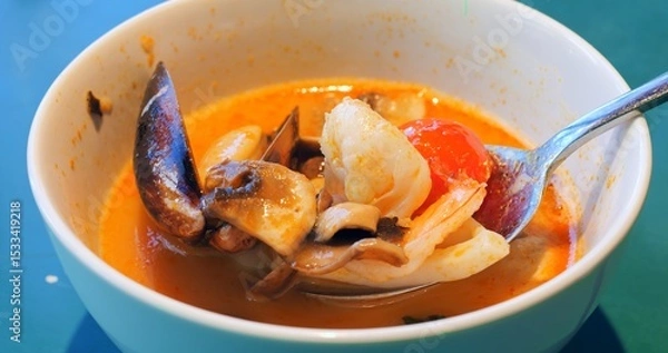 Obraz Spoon mixing and showing ingredients of a tom yum soup, a traditional spicy and sour thai soup, with seafood like shrimps, mussels, squid, and vegetables like mushrooms and tomatoes