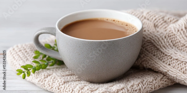 Fototapeta Warm cup of coffee in gray ceramic mug resting on cozy knitted beige blanket with small green plant nearby, evoking comfort and calm
