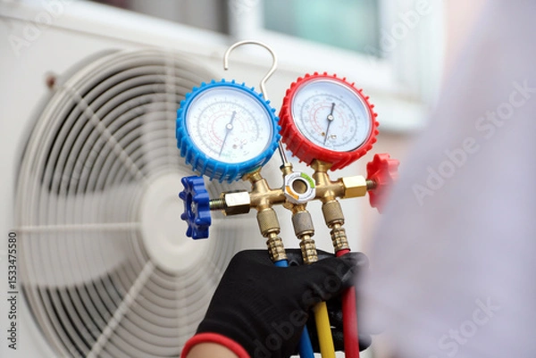 Fototapeta Air conditioning electrical technician using manifold gauge measuring tool checking refrigerant pump filling home air conditioner and maintenance heat fix repair and clean outdoor compressor unit.